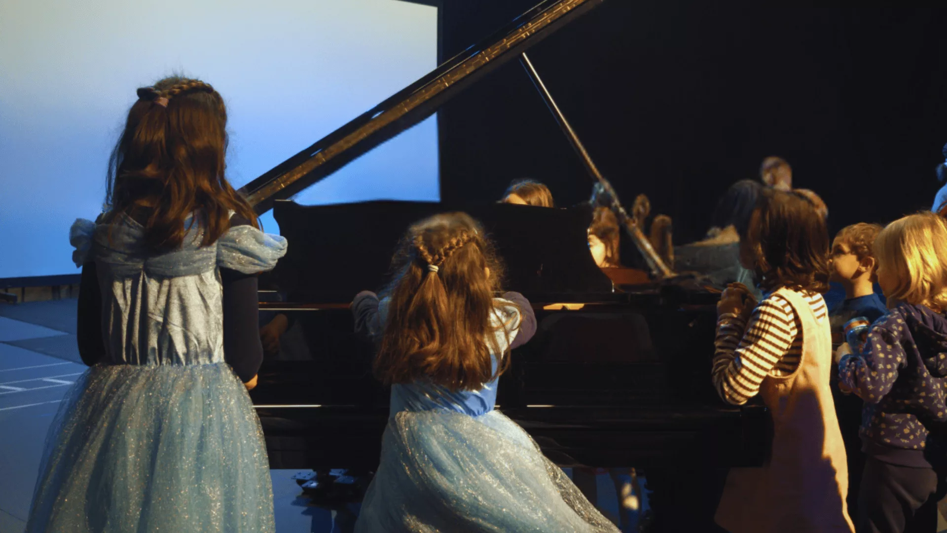 Due bambine travestite da Cenerentola di spalle sedute al pianoforte